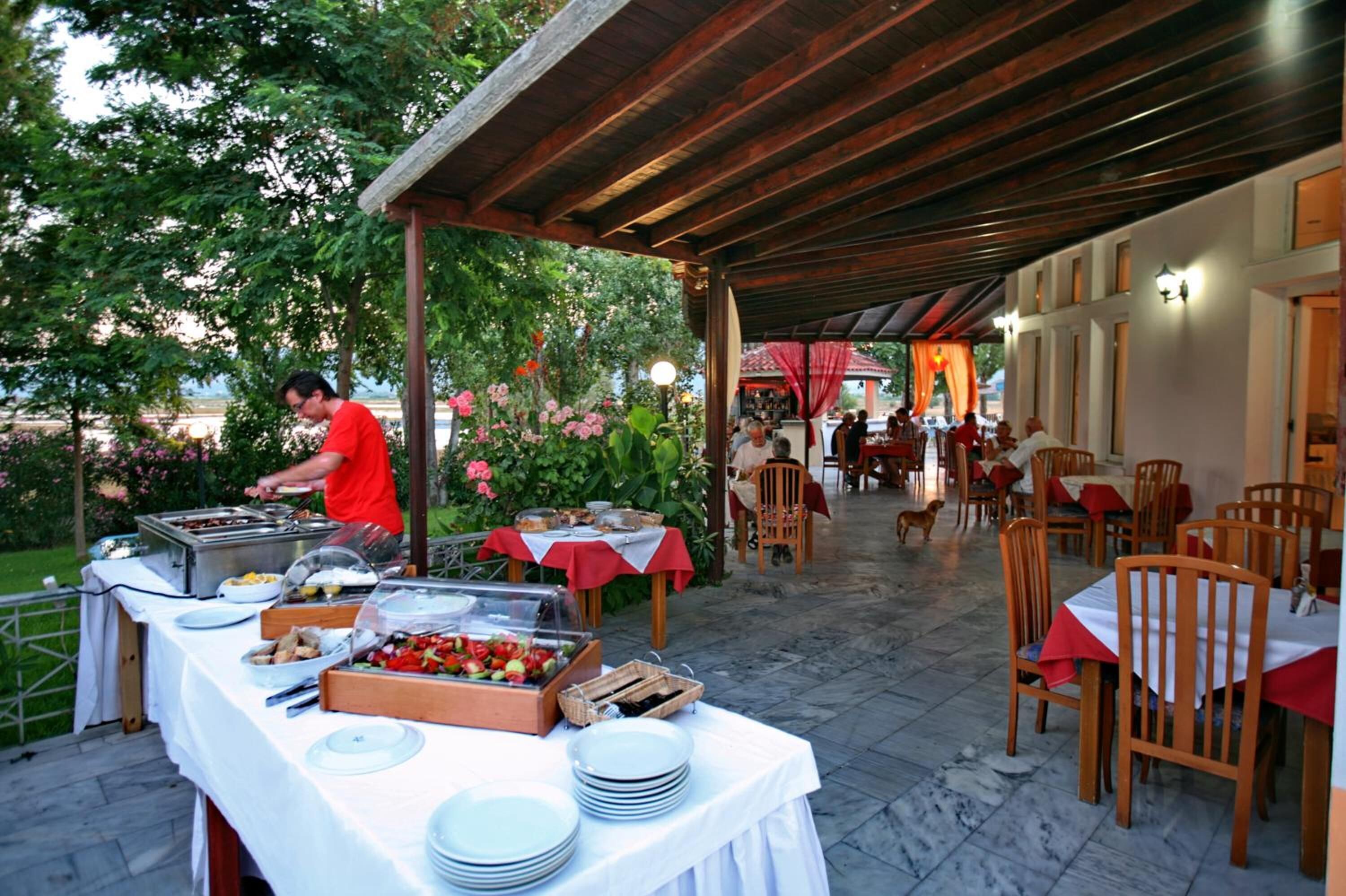 Uma área de refeições ao ar livre com mesas, cadeiras, um buffet e uma galeria coberta.