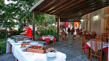 Uma área de refeições ao ar livre com mesas, cadeiras, um buffet e uma galeria coberta.