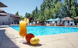 A poolside setting with a drink, an orange, and a lemon on the edge of the pool. - Aegeon Hotel (Lesvos)