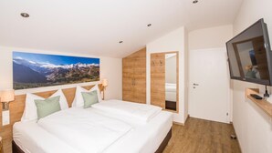 A modern hotel room with a large bed, wooden wardrobe, a TV, and a mountain landscape painting on the wall. - Appartements Auszeit (Lend)