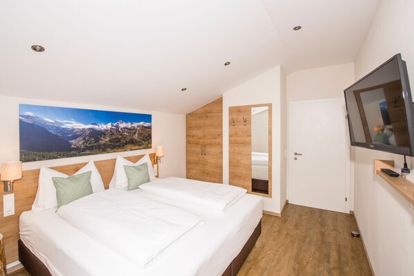 Habitación de hotel moderna con una cama grande, un armario de madera, un televisor y un cuadro de un paisaje montañoso en la pared.