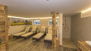 A spa room with four sun loungers, a wooden column, a shower area, and a wall-mounted picture of a mountain landscape. - Appartements Auszeit (Lend)