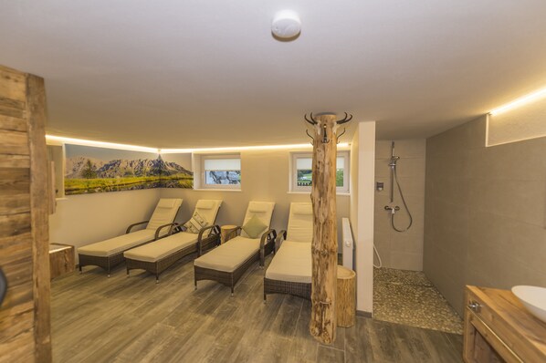 A spa room with four sun loungers, a wooden column, a shower area, and a wall-mounted picture of a mountain landscape. - Appartements Auszeit (Lend)