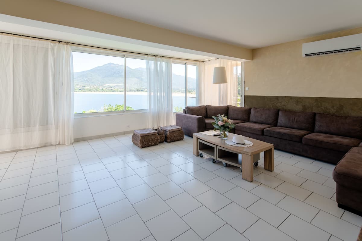 Uma sala de estar moderna com uma janela grande, um sofá marrom, uma mesa de centro de madeira e cestos de armazenamento em vime.