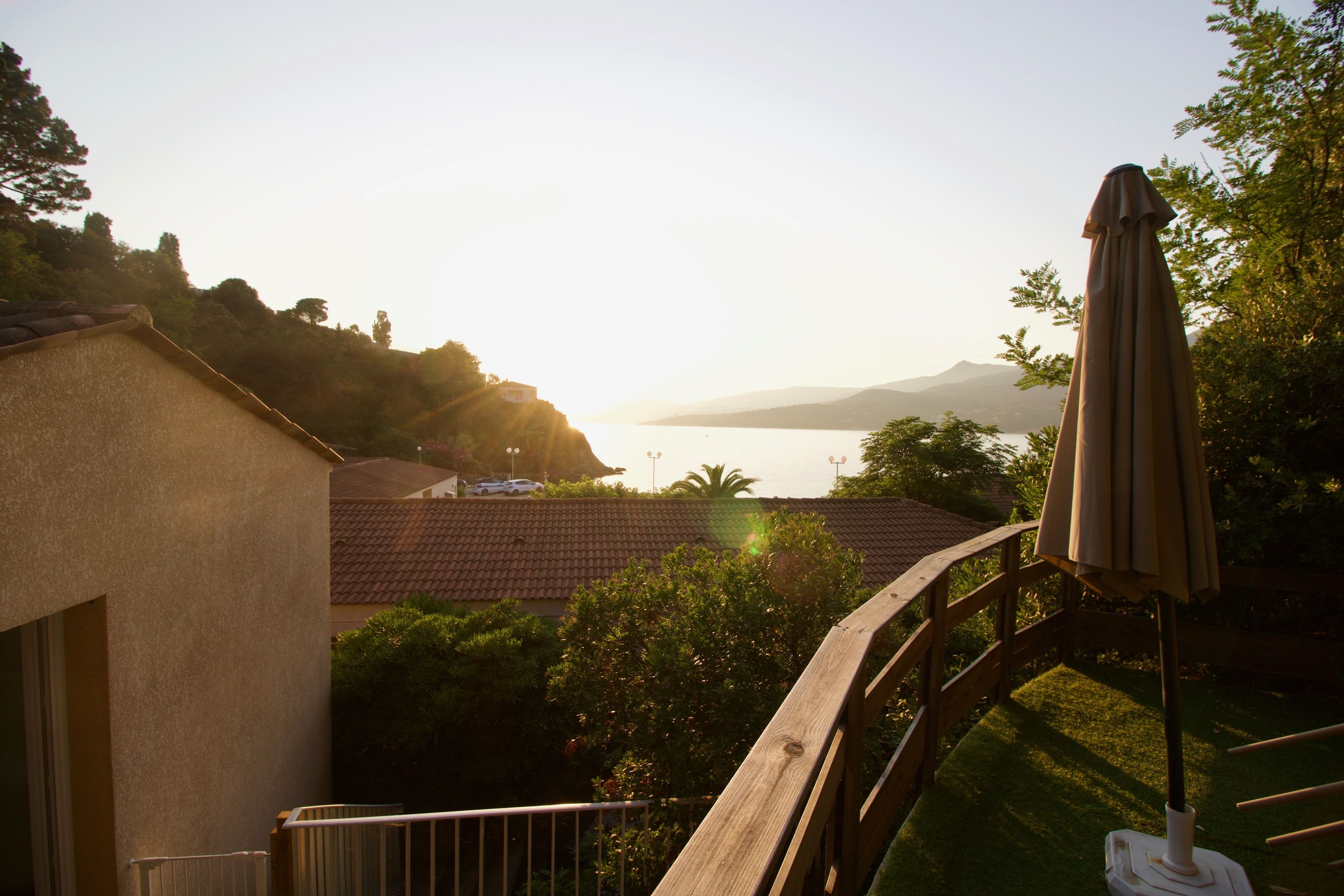 A view of a balcony with a wooden railing, overlooking a body of water and distant mountains.