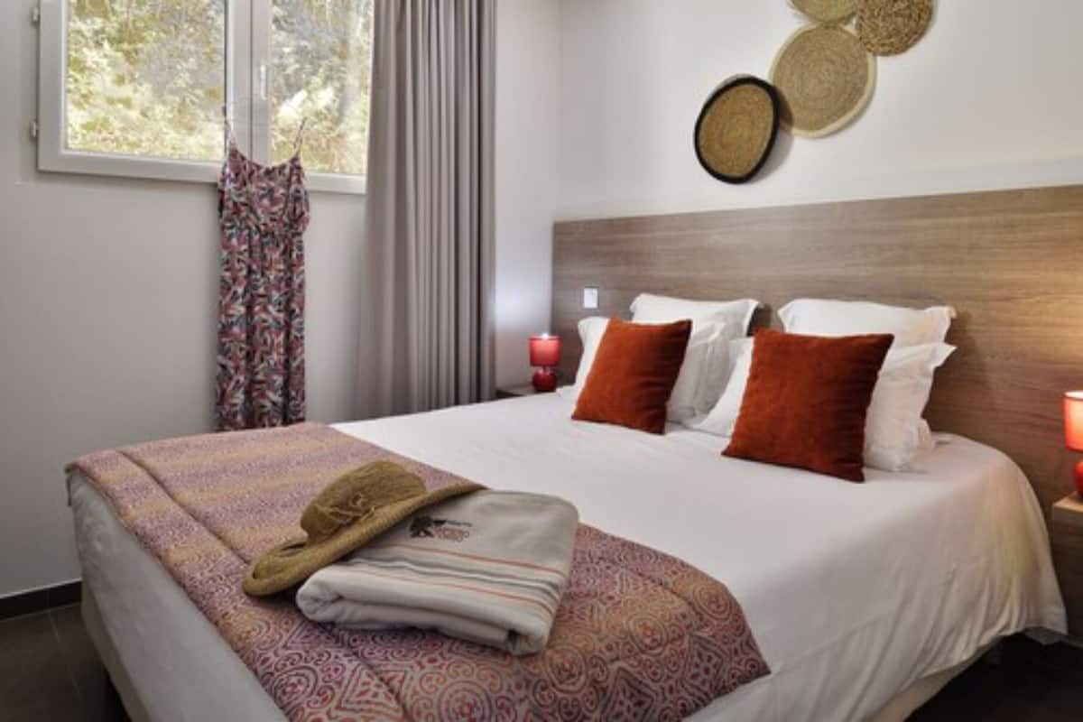 Uma cama bem arrumada com roupa de cama estampada, cabeceira e mesa de cabeceira com uma vela.