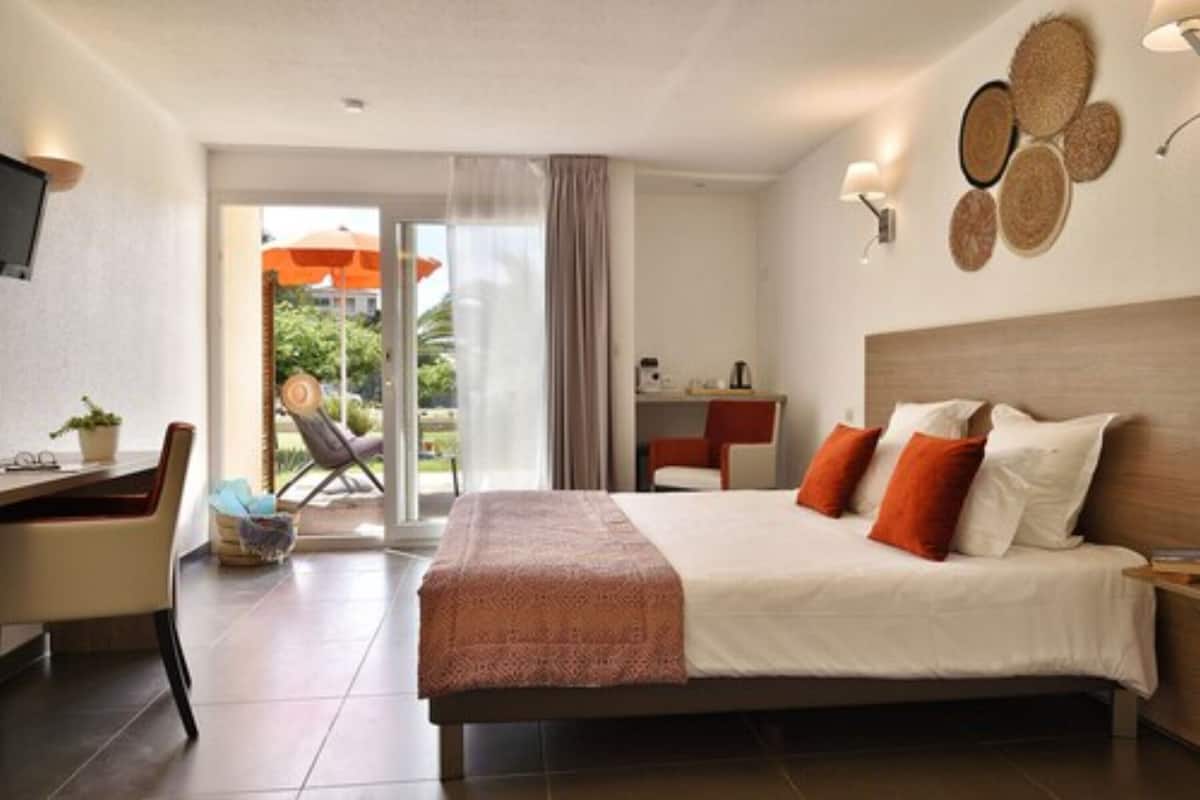 Quarto de hotel com cama, escrivaninha, cadeira e vista para o exterior.