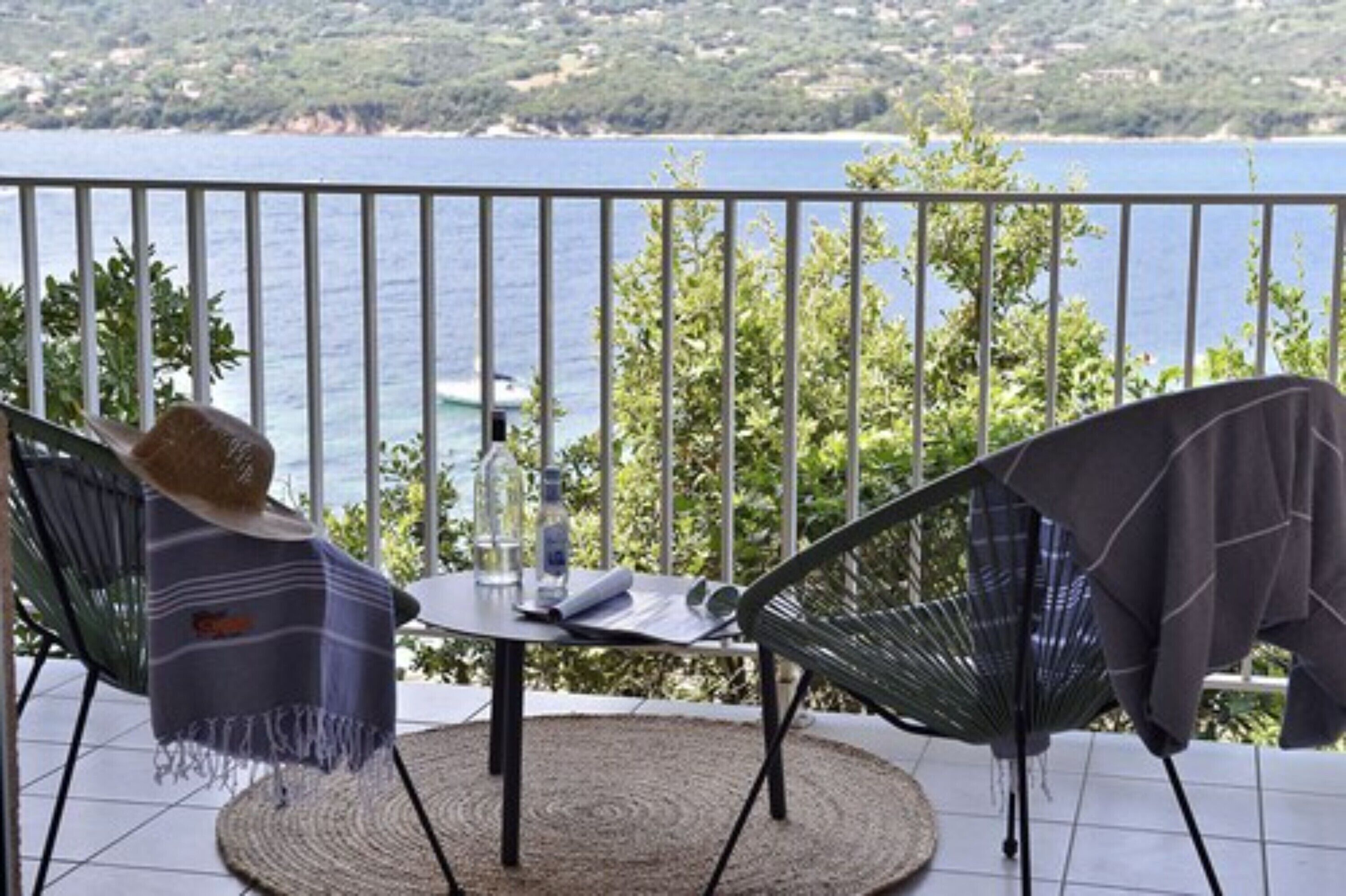 A balcony with two chairs, a table, and a view of the sea.