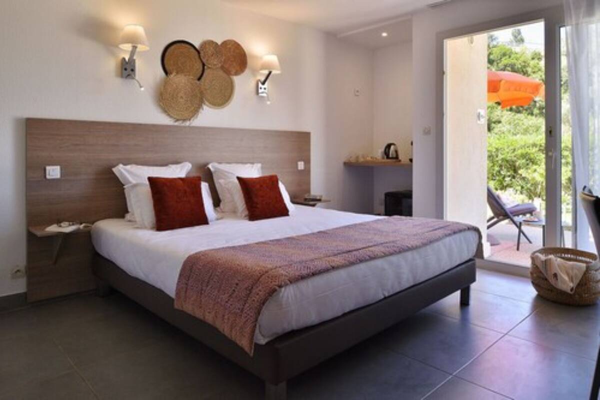 Quarto moderno com uma cama grande, uma mesinha de cabeceira, uma luminária na parede e vista para o exterior.