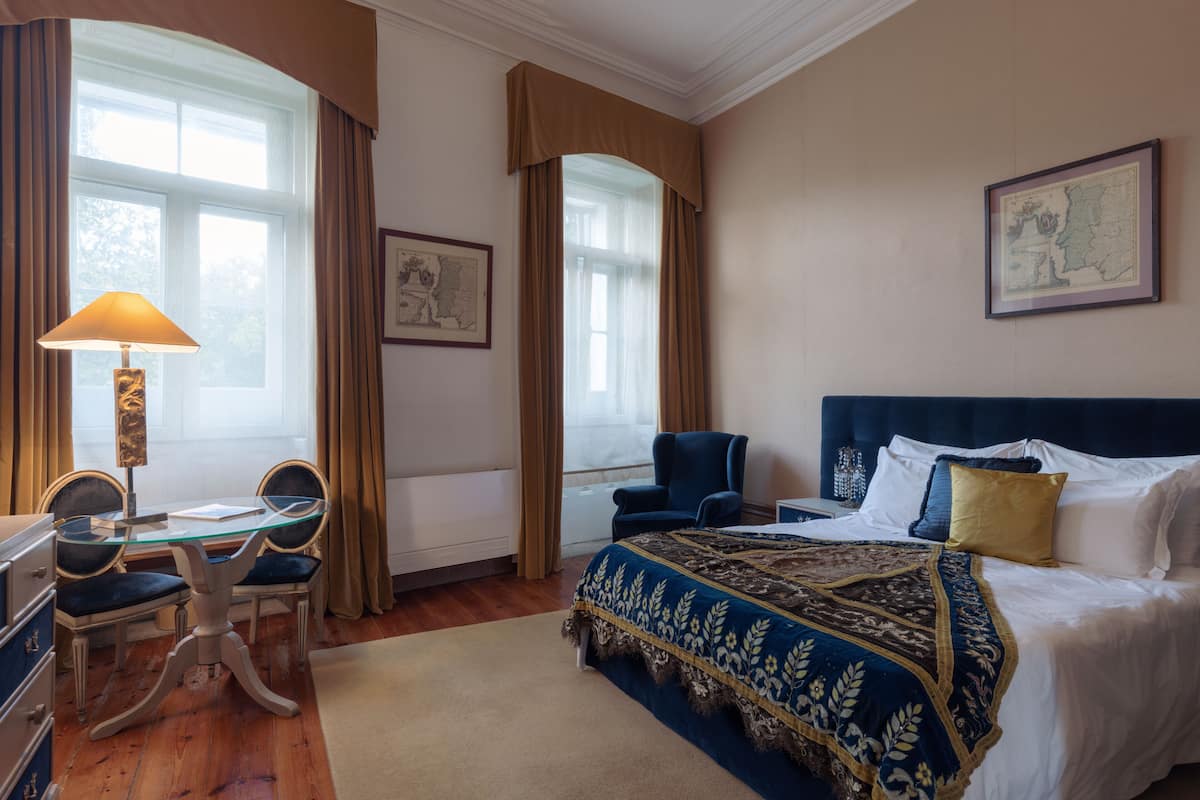 A hotel room with a bed, a desk with a lamp, a chair, and a map on the wall.