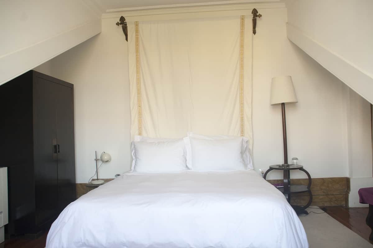 A neatly made bed in a hotel room with a high ceiling and a large window.
