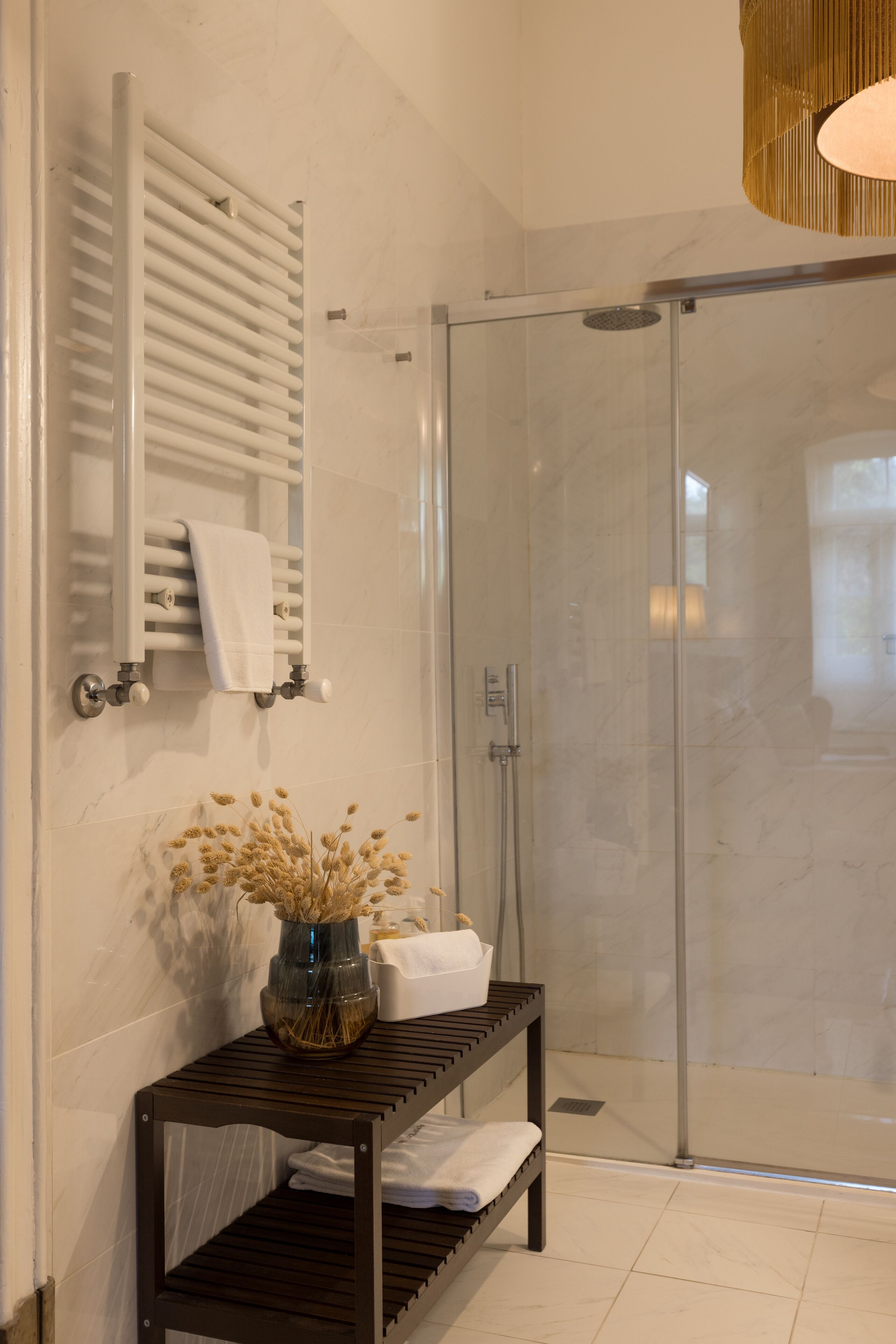 Ein modernes Badezimmer mit Duschkabine aus Glas, Handtuchhalter und einem Holzregal mit einer Vase getrockneter Blumen.