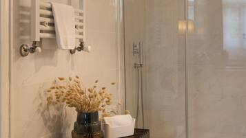 Ein modernes Badezimmer mit Duschkabine aus Glas, Handtuchhalter und einem Holzregal mit einer Vase getrockneter Blumen.