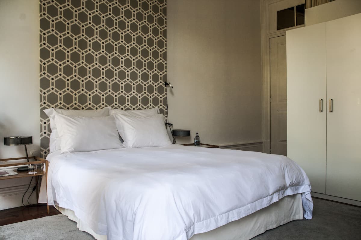 A neatly made bed with white linens, a bedside table with a lamp, and a wardrobe with two doors.