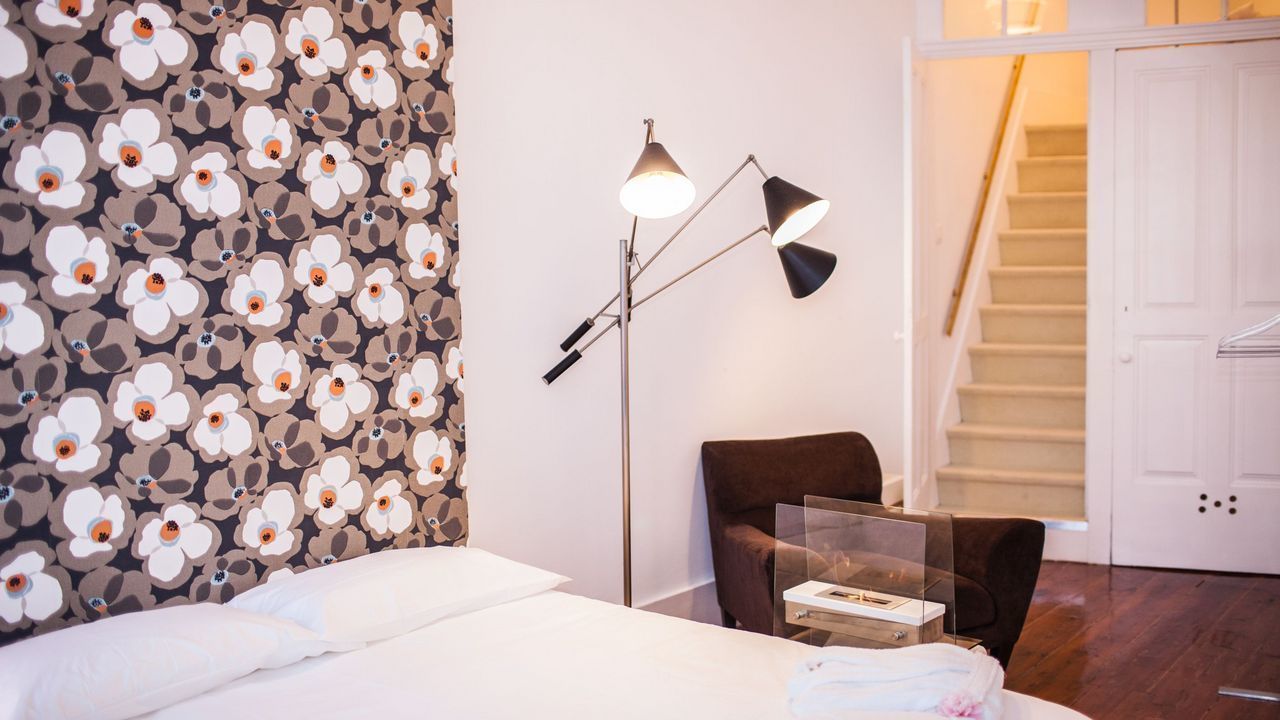 Een hotelkamer met een bed, een bureau met een laptop, een stoel, een vloerlamp en een trap.