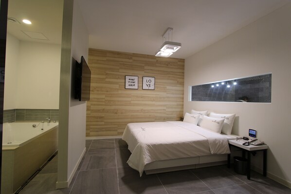 A modern bedroom with a large bed, a bedside table with a phone, a wall-mounted TV, and a wooden accent wall with motivational quotes.