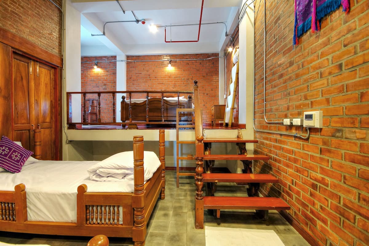 A room with a wooden bed, a desk, and a brick wall.