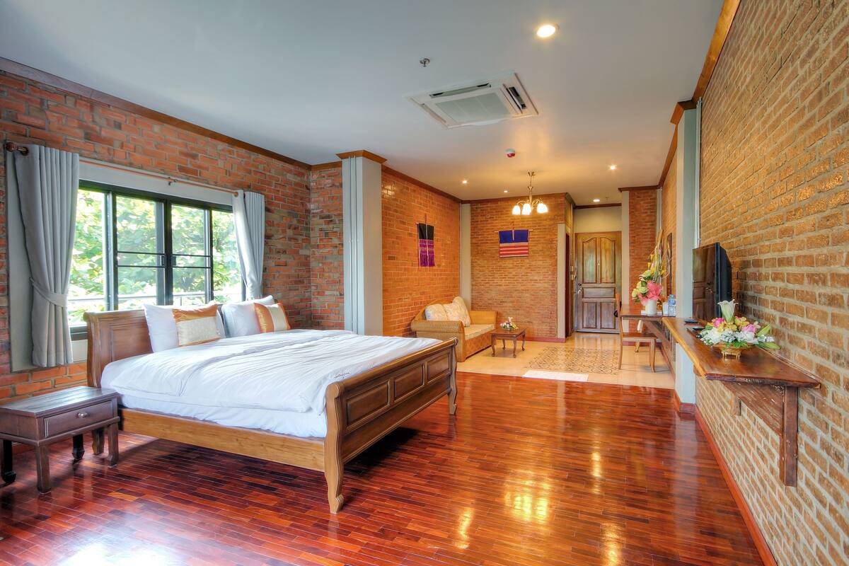 A spacious bedroom with a large bed, a wooden nightstand, a desk with a chair, and a small table with flowers.
