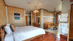 A bedroom with a wooden bed, brick walls, a wooden floor, a ceiling fan, and a wooden dresser with a towel hanging on it.