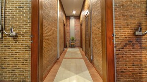 A narrow hallway with brick walls and wooden doors, leading to a room with a tiled floor and a small table with a plant.