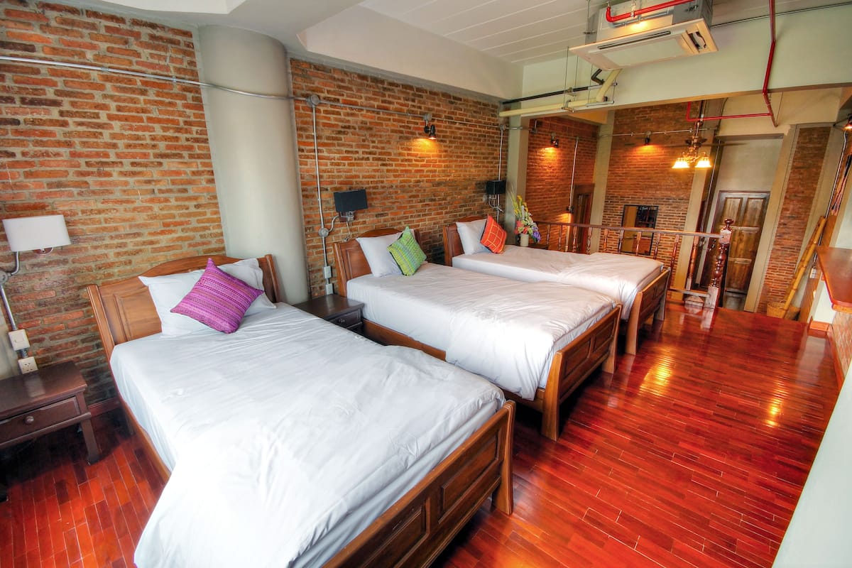 A hotel room with two beds, wooden flooring, brick walls, and a loft area.
