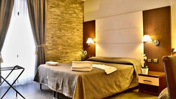 Une chambre d’hôtel avec un lit, des tables de chevet, une lampe, un téléviseur fixé au mur et une fenêtre avec des rideaux.