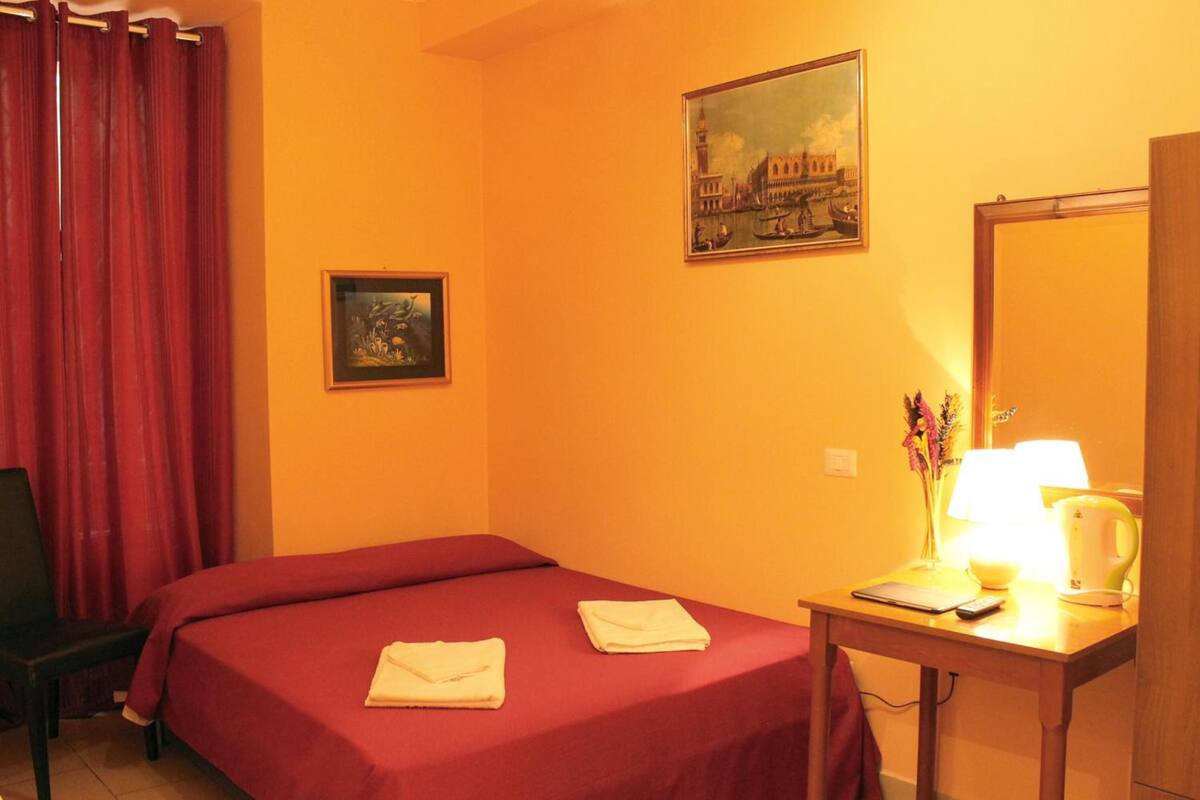 A hotel room with two beds, a desk with a lamp, a mirror, and a painting on the wall.