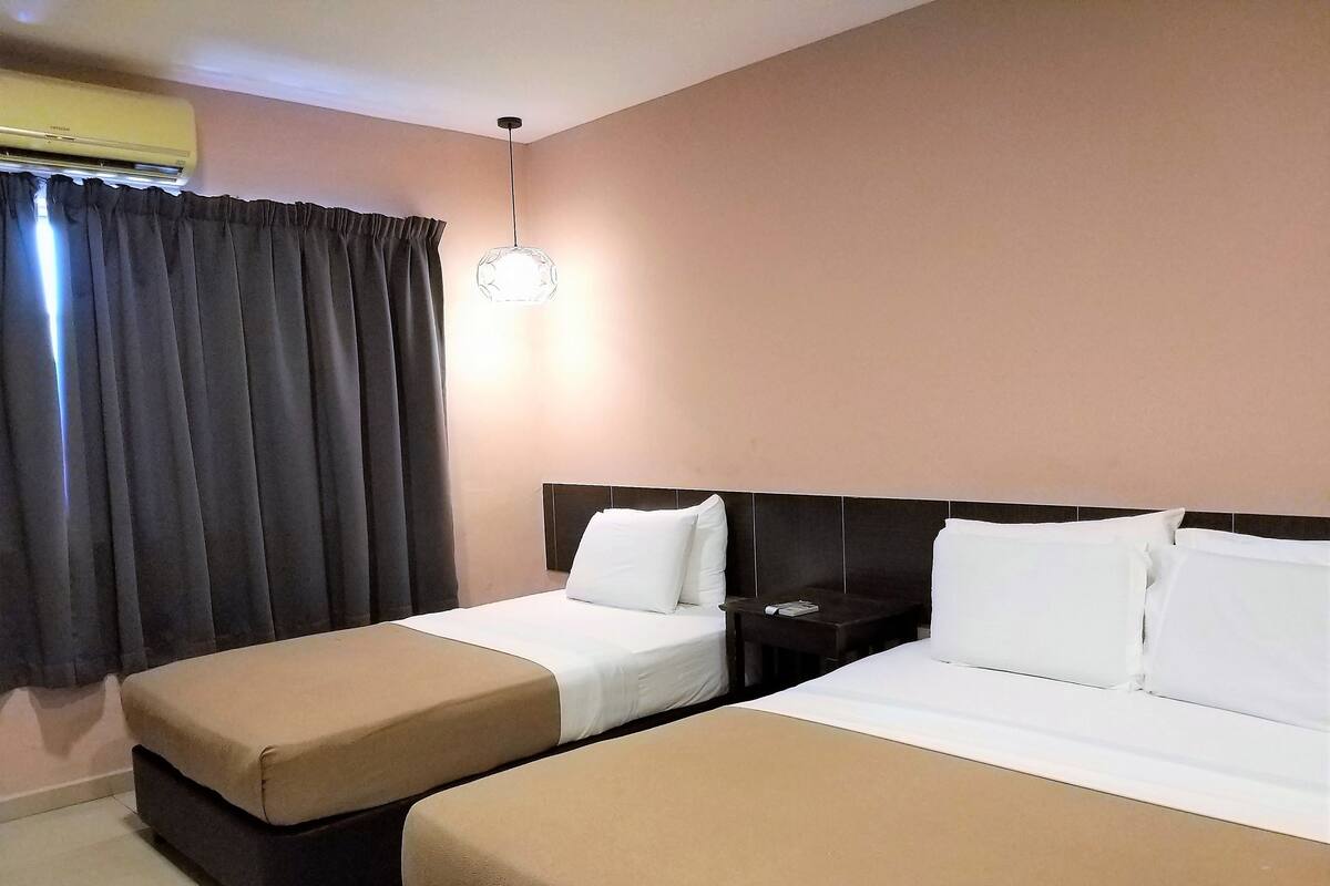 Ein Hotelzimmer mit zwei Betten, einem Nachttisch, einer Lampe und einer Klimaanlage.