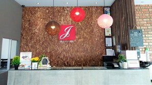 A reception desk with a wooden backdrop, a prominent 'J' logo, and various informational signs and decorations. - Hotel Jelai Mentakab (Mentakab)