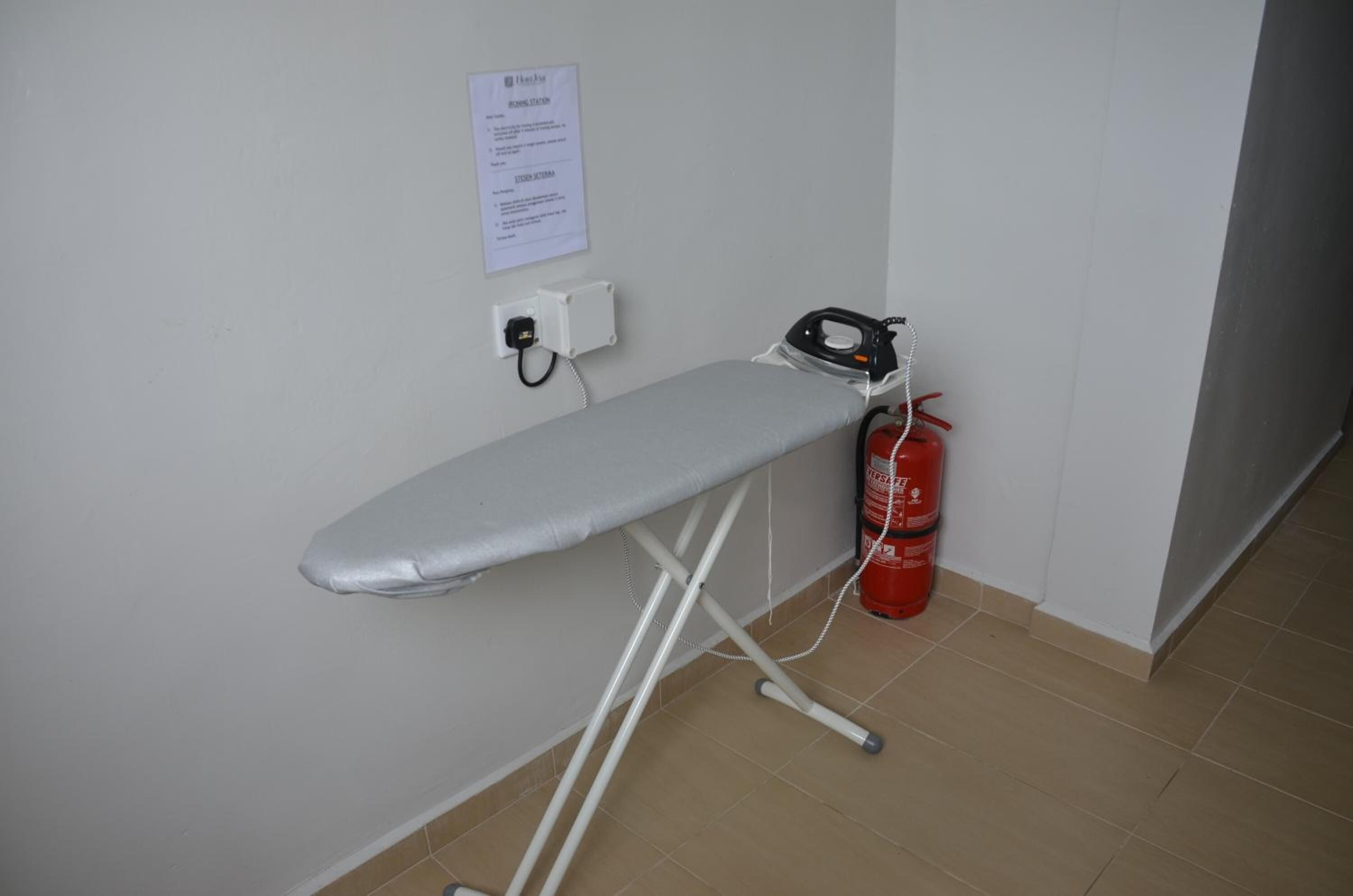 Una habitación con una tabla de planchar fijada a la pared, un extintor y un enchufe.