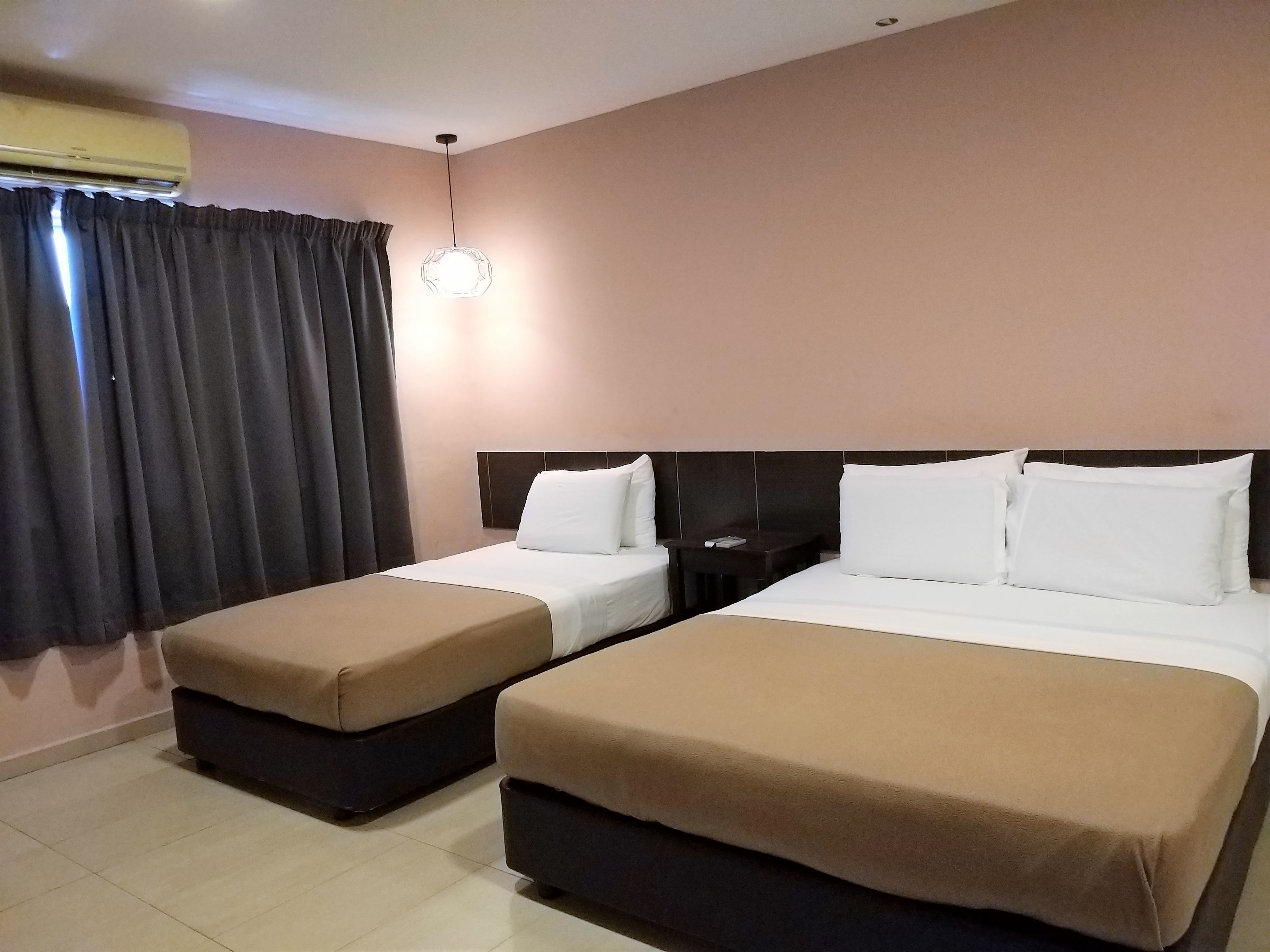 A hotel room with two beds, a nightstand, a lamp, and a window with curtains.