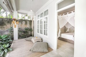 A bedroom with a bed, a window, a small table, and a decorative item on the wall. - Villa Lodek Deluxe (Seminyak)