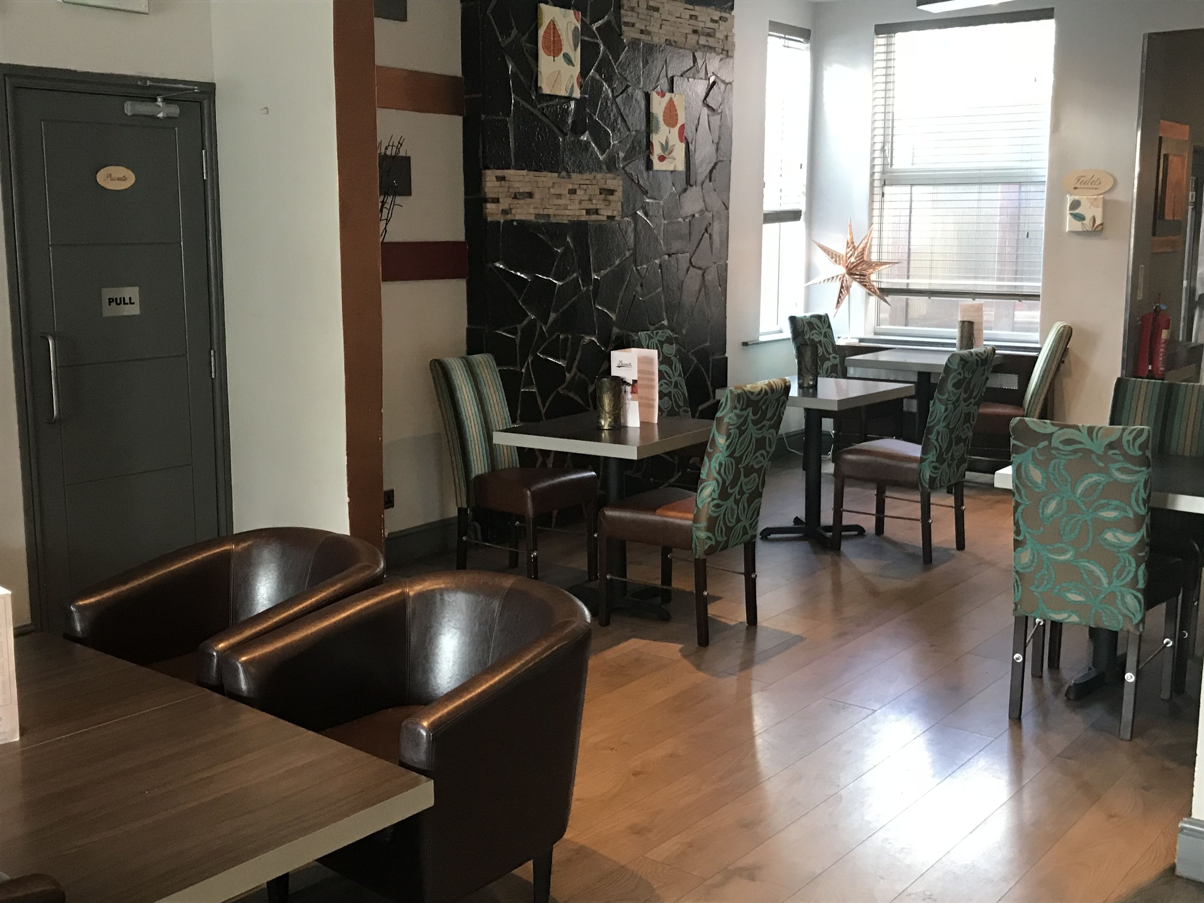 A restaurant interior with a stone wall, wooden flooring, and a mix of upholstered and leather chairs.