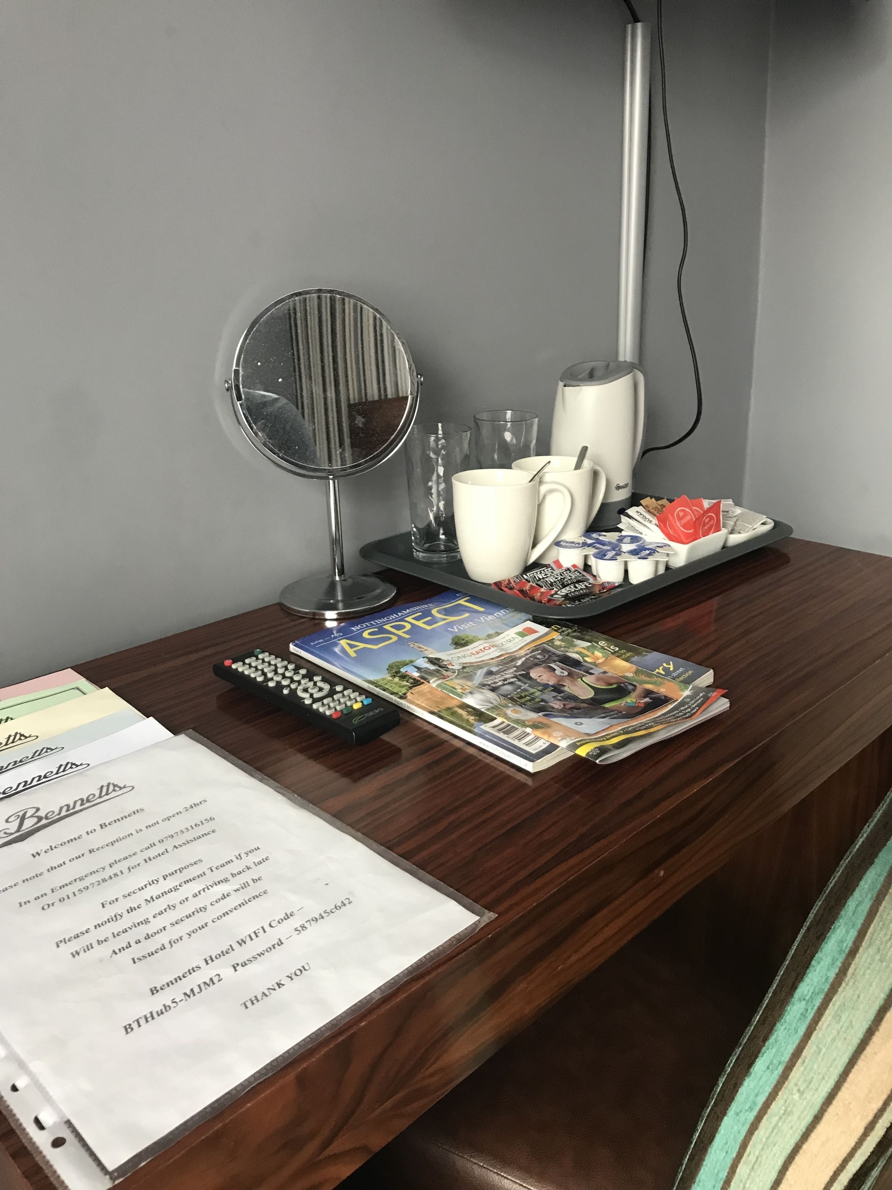 A hotel reception desk with a mirror, a lamp, a tray with cups and a remote control, and a magazine.