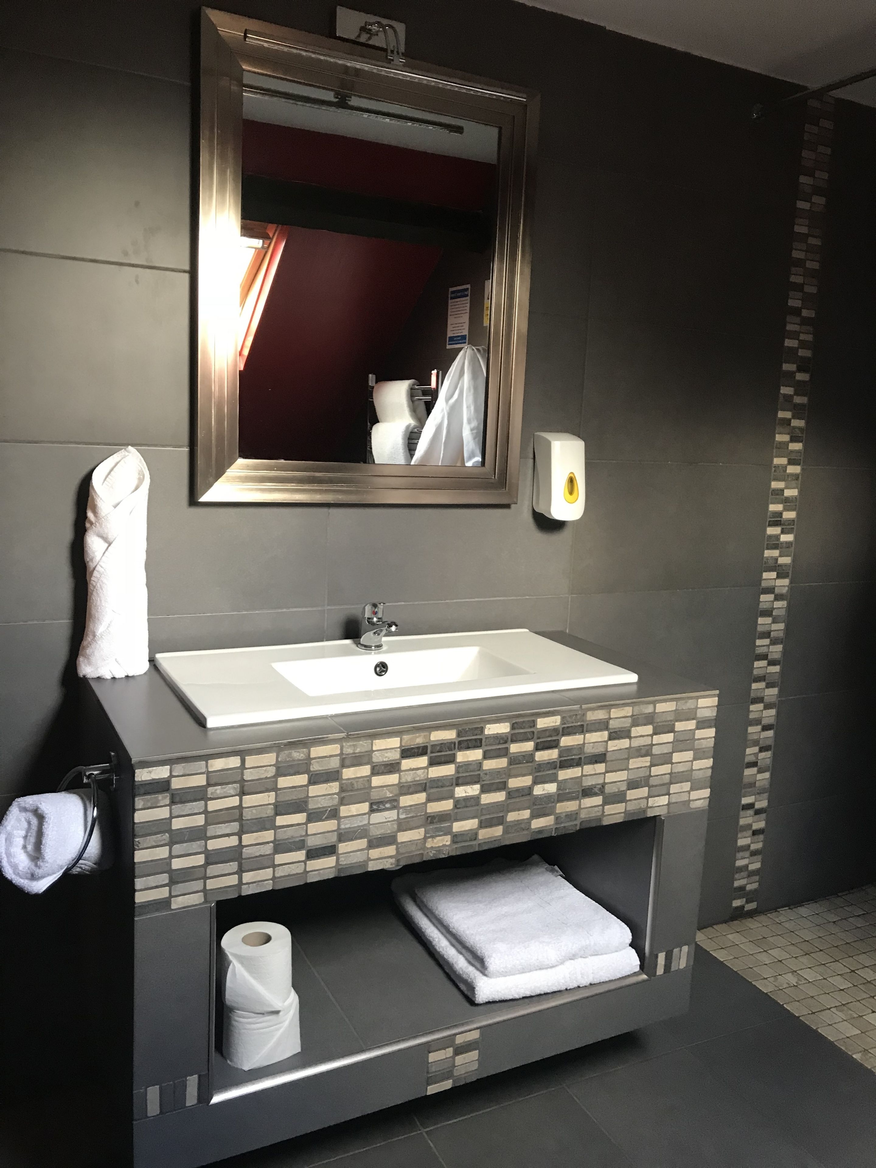Un baño con un lavabo blanco, un espejo, un perchero y un dispensador de jabón.
