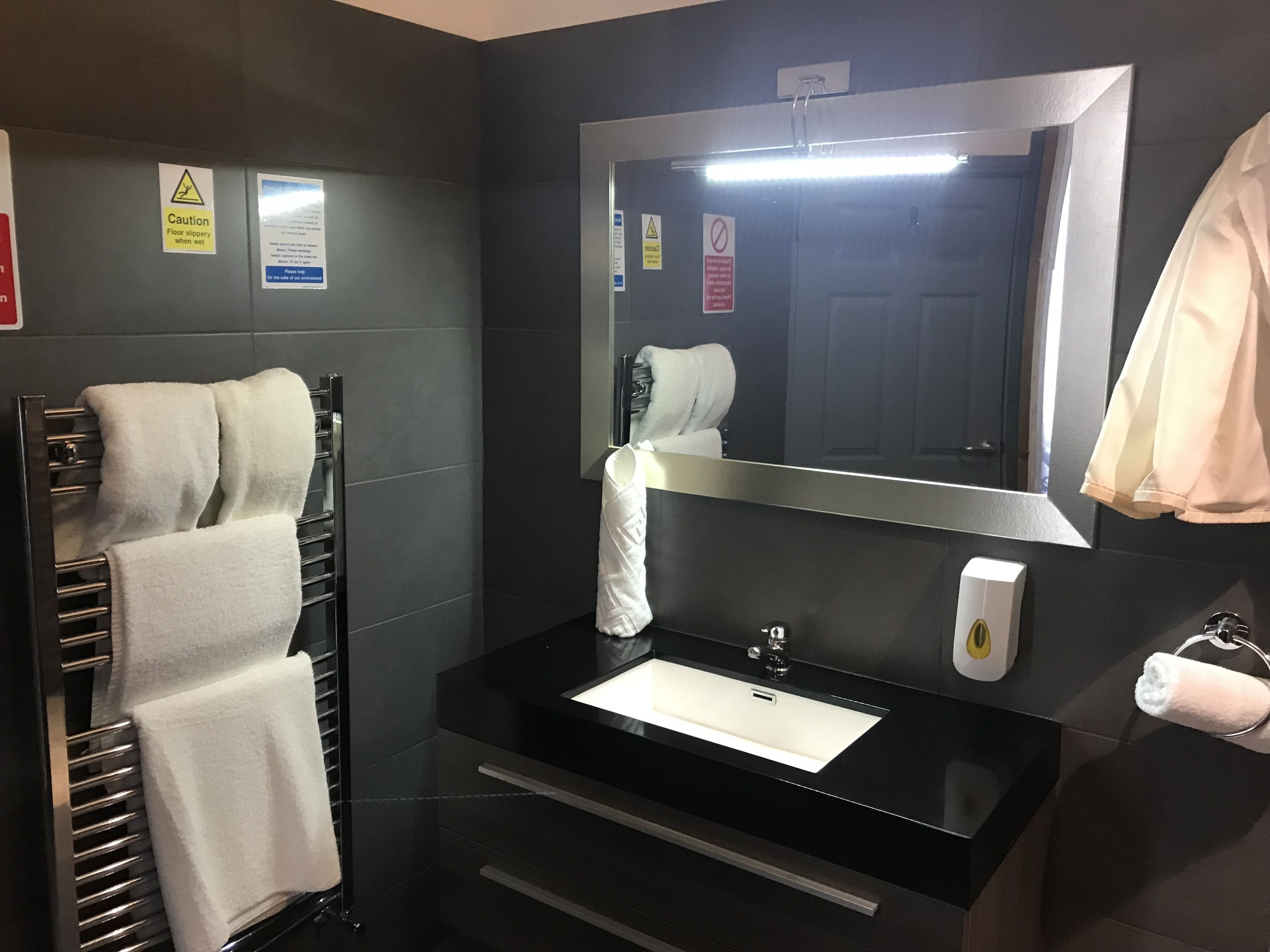 A modern bathroom with a black sink, a mirror, a towel rack, and a toilet paper holder.