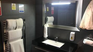 A modern bathroom with a black sink, a mirror, a towel rack, and a toilet paper holder.