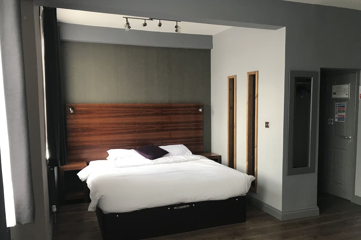 A modern bedroom with a wooden headboard, a bed with white linens, and a dark wooden floor.