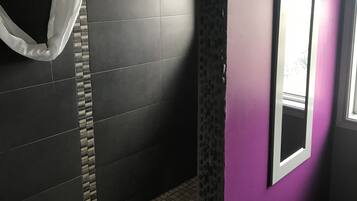 Ein Badezimmer mit dunkel gefliesten Wänden, einer Duschkabine, einem Fliesenboden und einem Fenster mit Blick.