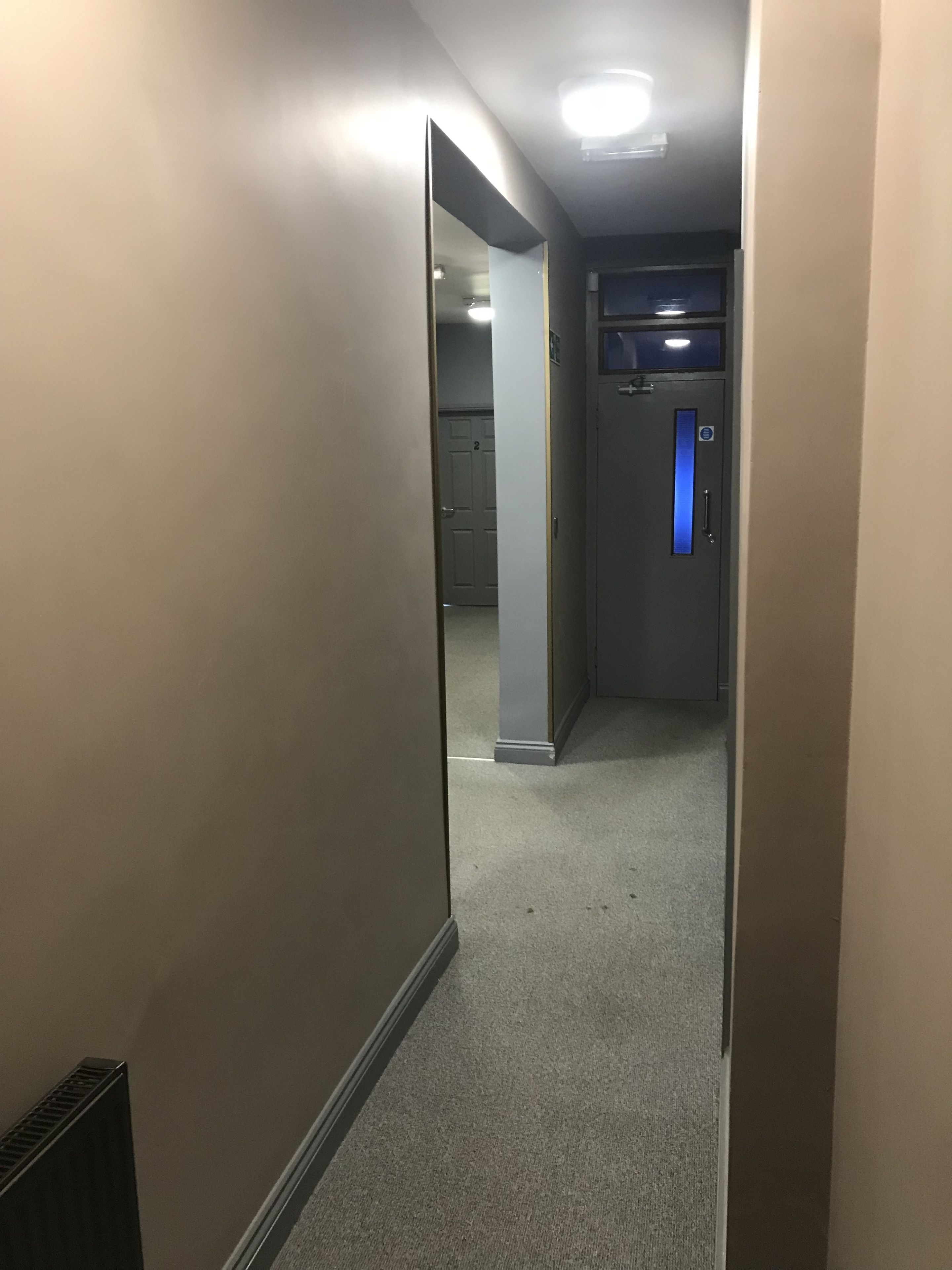 A hallway with carpeted floors, a door with a blue handle, and a vent on the left.