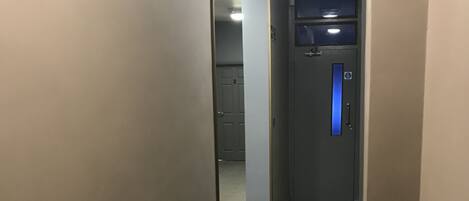A hallway with carpeted floors, a door with a blue handle, and a vent on the left.