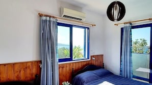 A room with two beds, wooden paneling, a small table with a plant, and a view of greenery through large windows. - Kanalli Restaurant & Apartments (Pomos)