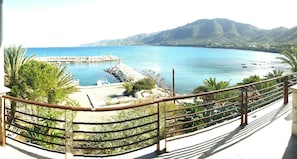 Une vue sur la côte depuis un balcon doté d’une balustrade, une zone rocheuse avec une petite piscine, et une montagne en arrière-plan.