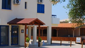 A building with blue shutters, an air conditioning unit, a covered entrance, and a sign indicating parking. - Kanalli Restaurant & Apartments (Pomos)