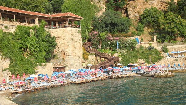 A riverside hotel with a terrace overlooking the water, a pool area with sun loungers and umbrellas, and a stone wall with vegetation. - Kosa Butik Otel (Antalya)