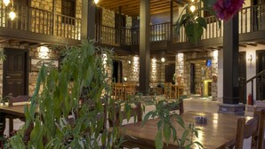 A spacious indoor area with wooden tables and chairs, stone walls, and a balcony with railings. - Kosa Butik Otel (Antalya)