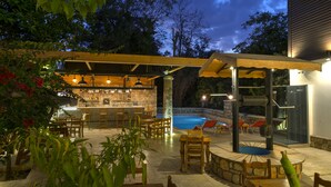 An outdoor bar area with stone walls, wooden furniture, and a pool. - Kosa Butik Otel (Antalya)