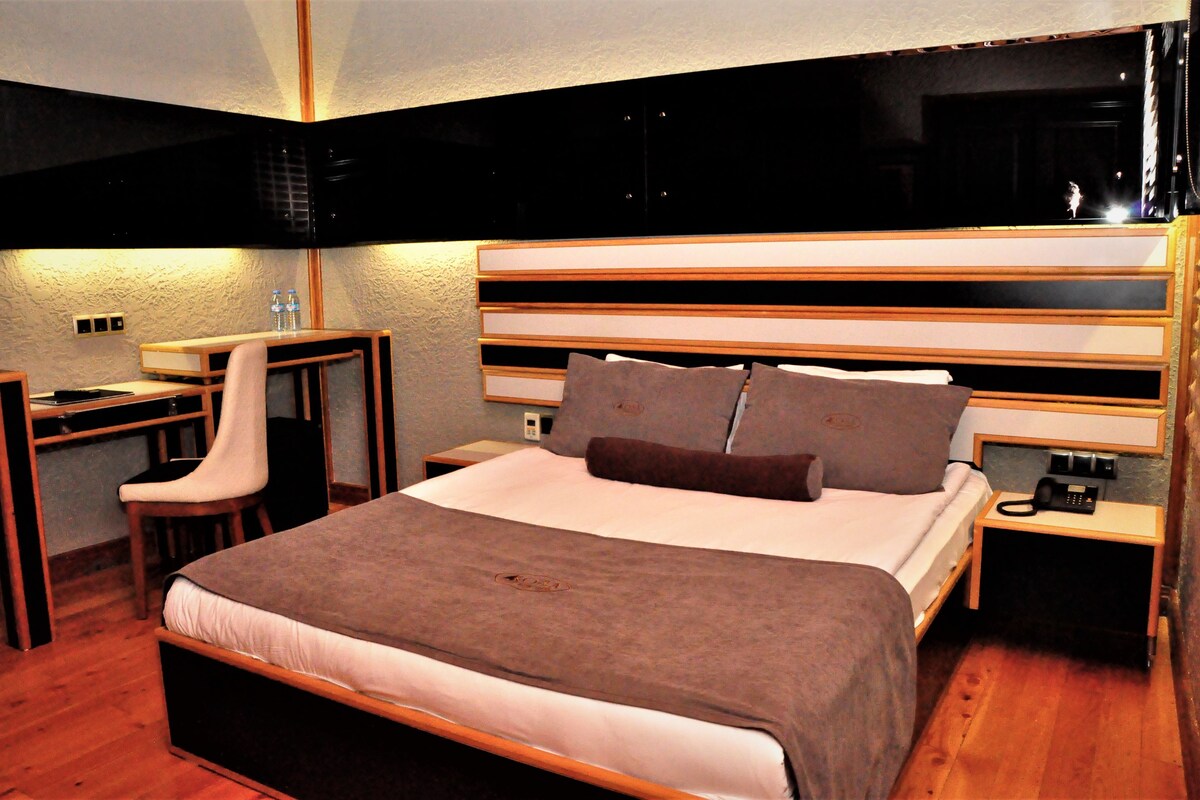 A bedroom with a bed, bedside table, chair, desk, and a small table with a lamp.
