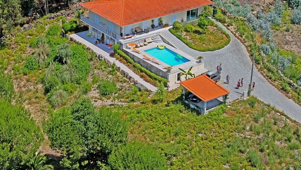 Ein Haus mit Schwimmbad, umgeben von üppiger Vegetation und einem roten Ziegeldach.