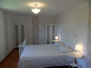 Een slaapkamer met een bed, twee nachtkastjes met lampen, een kroonluchter en een deur.
